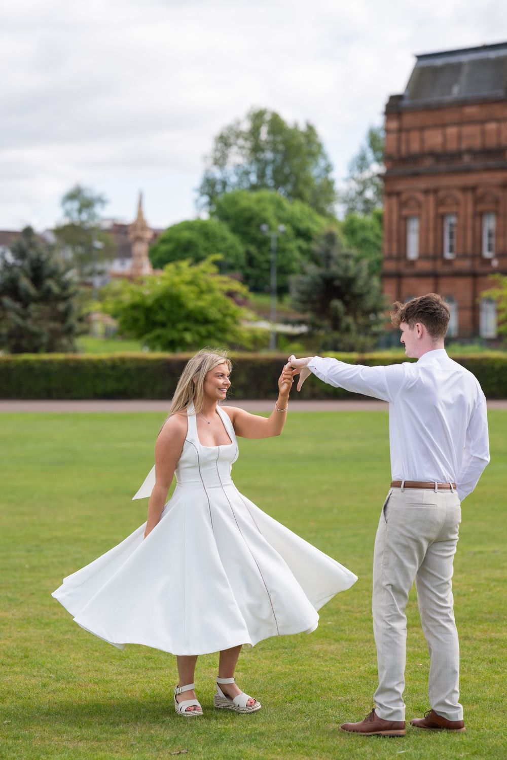 A couple dances on a lawn with a beautiful twirling white dress movement.