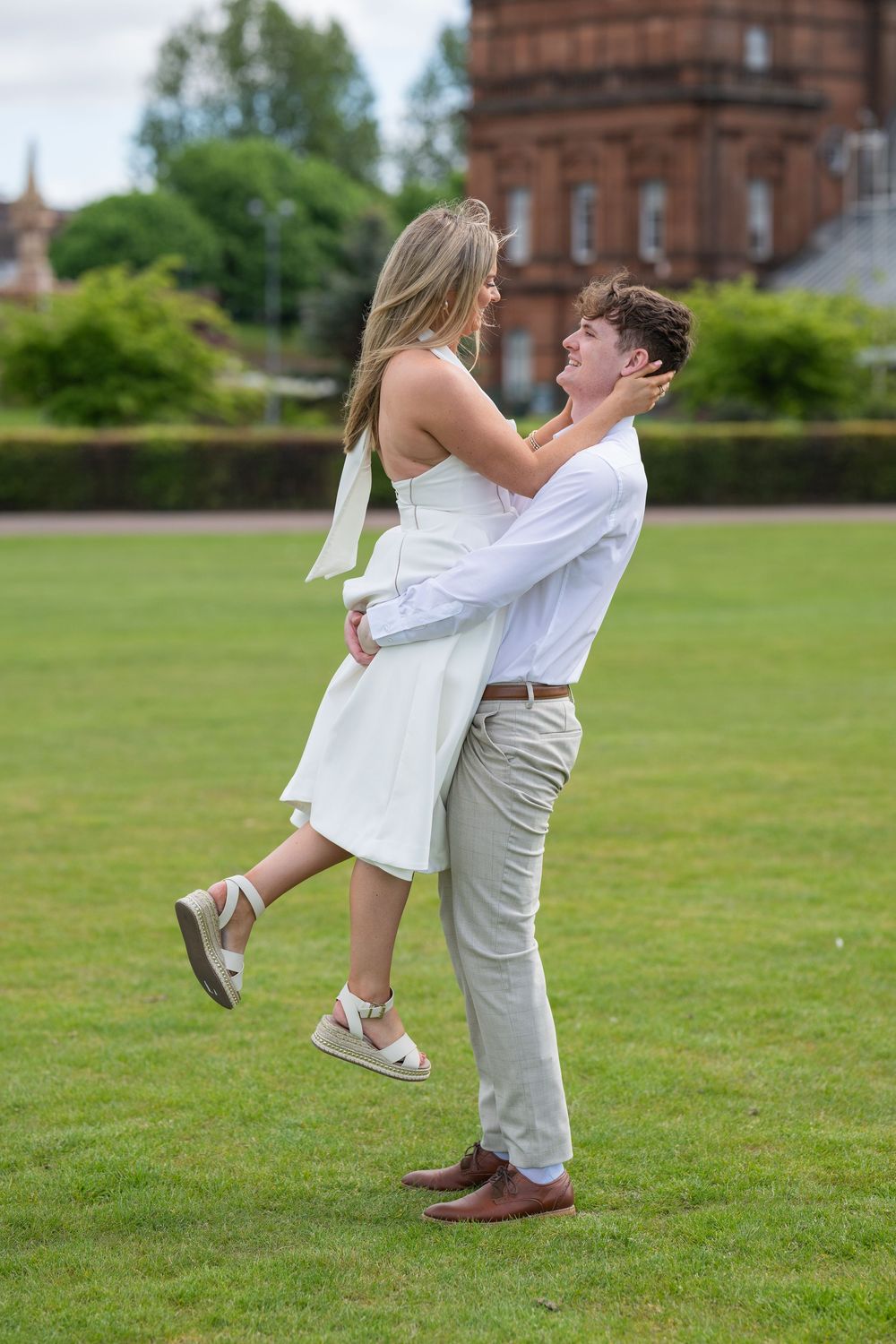 A playful lift pose on a grassy lawn with a historic brick building in the background.