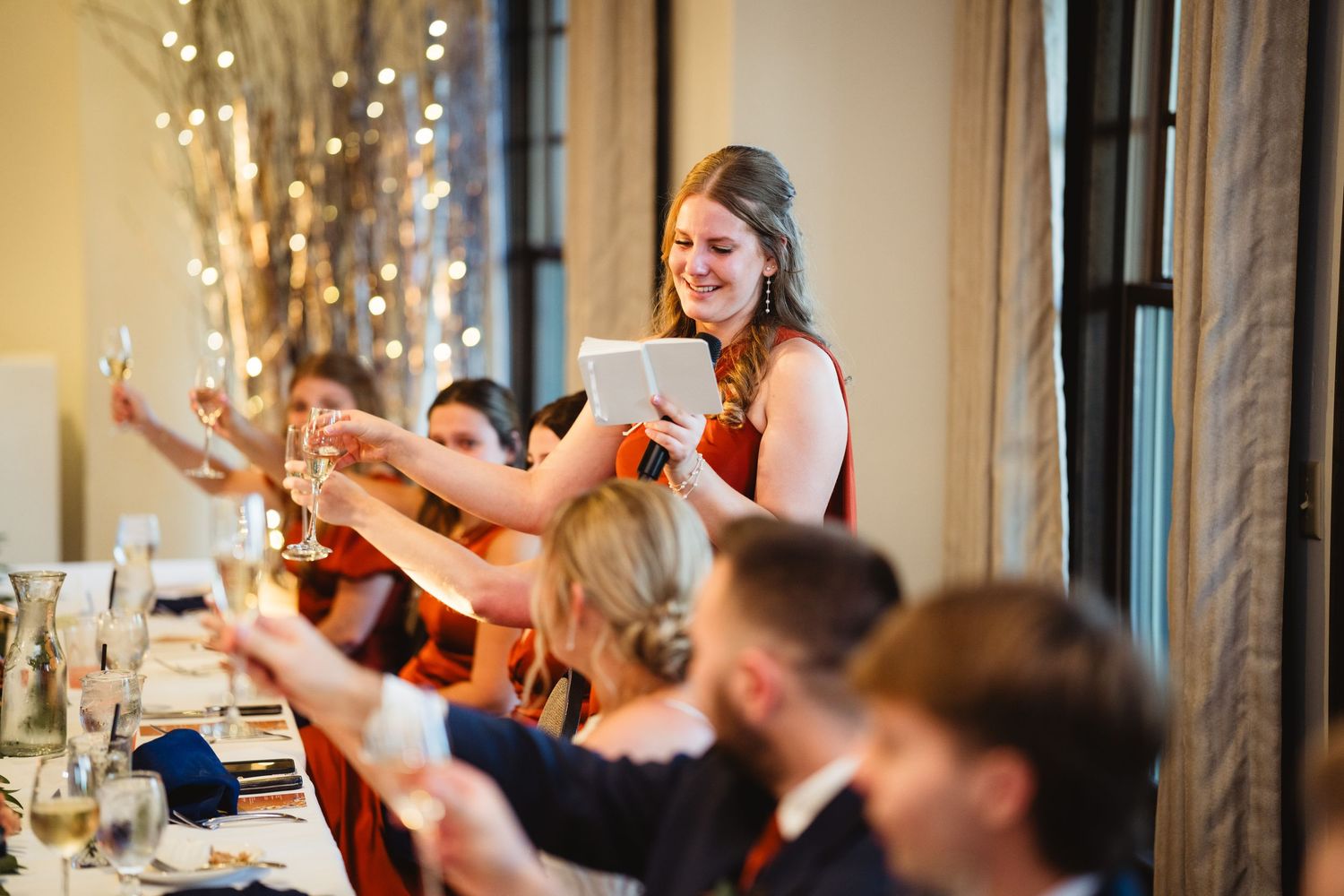 Wedding guests raise champagne glasses in a celebratory toast during an elegant indoor reception.