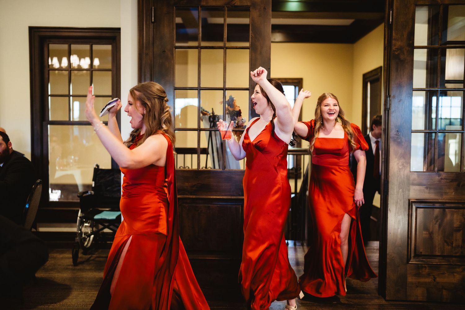 A group of bridesmaids in red dresses dance and celebrate during a wedding reception.