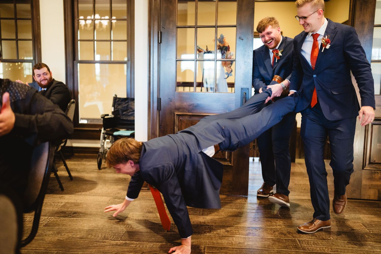 A group of groomsmen in navy suits playfully pose while doing pushups in a formal indoor setting.