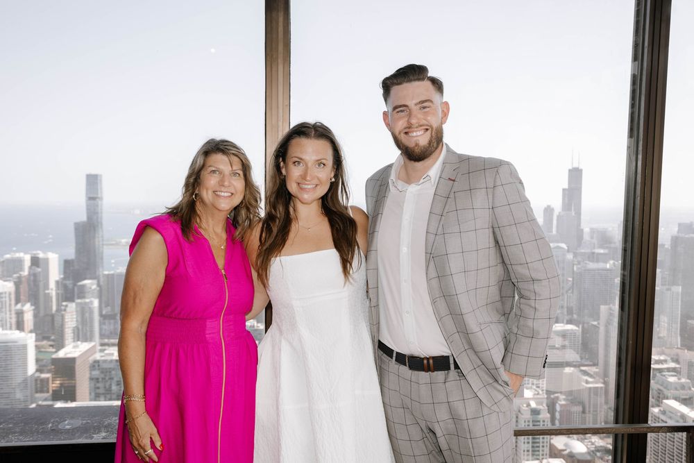 A group stands in a modern office space with floor-to-ceiling windows overlooking a city skyline.