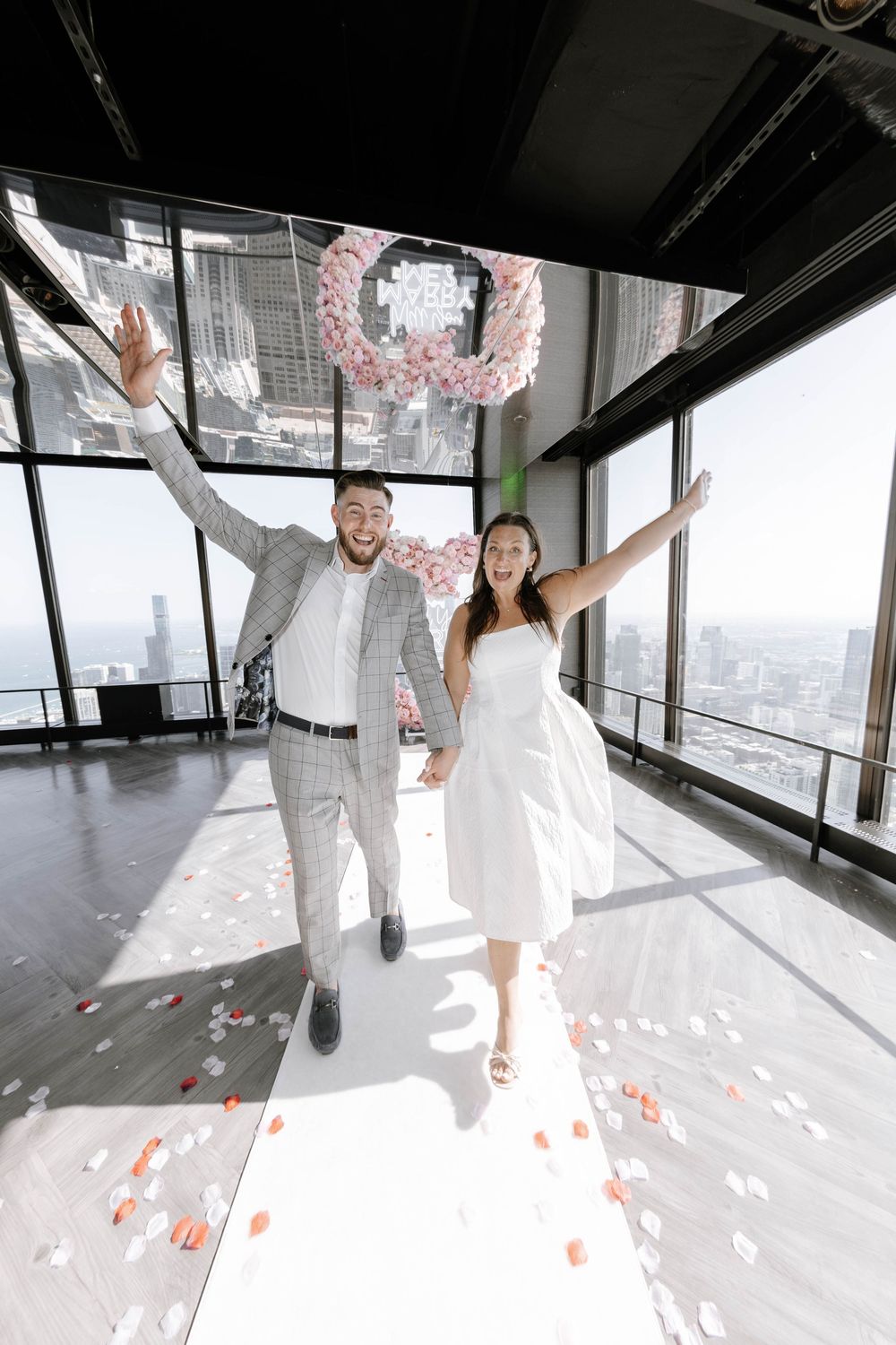 Wedding couple walking in modern building with pink rose petals scattered on floor.