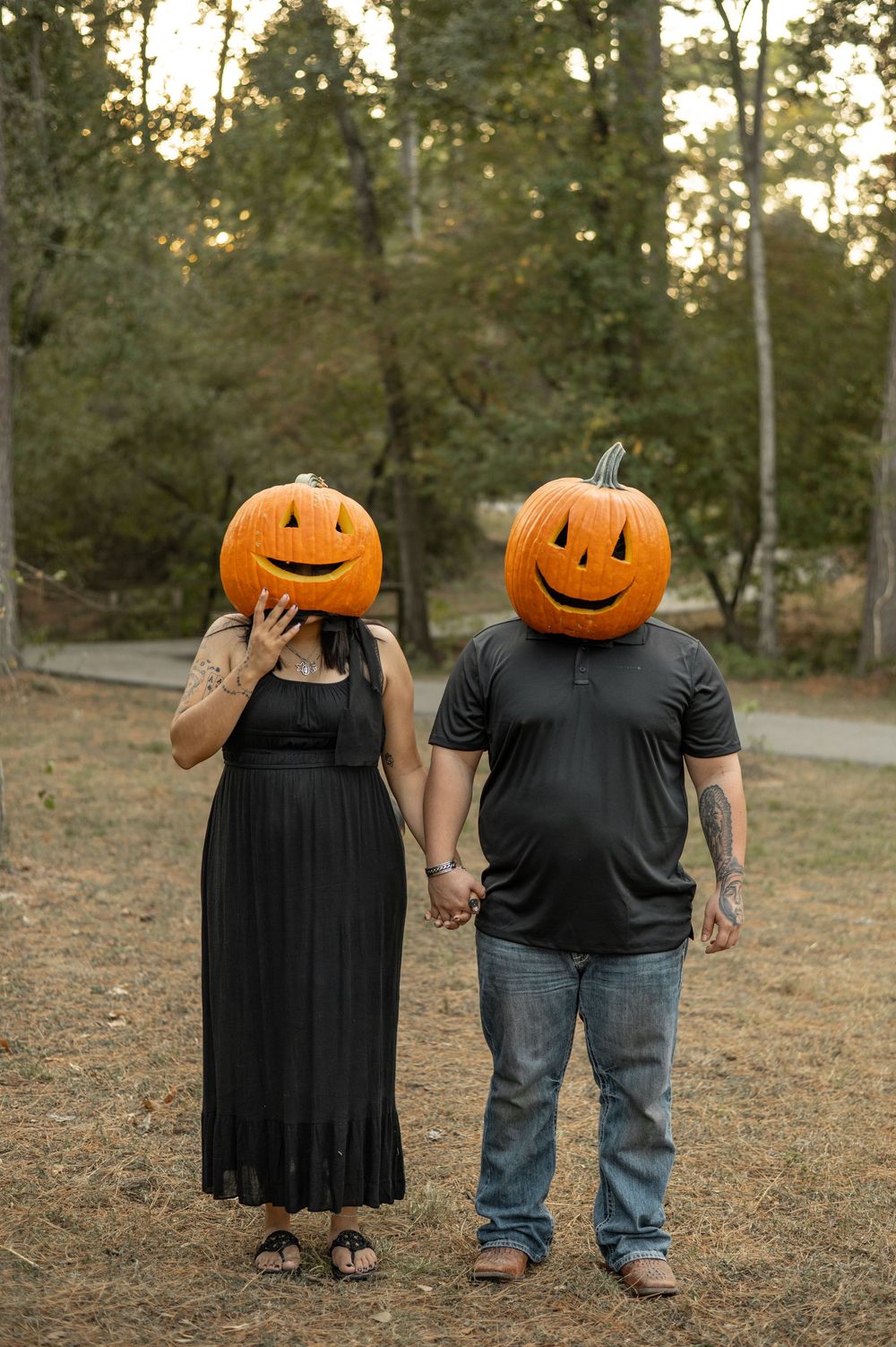 Creative Halloween couple photoshoot with jack-o'-lantern pumpkin heads in an autumn outdoor setting.