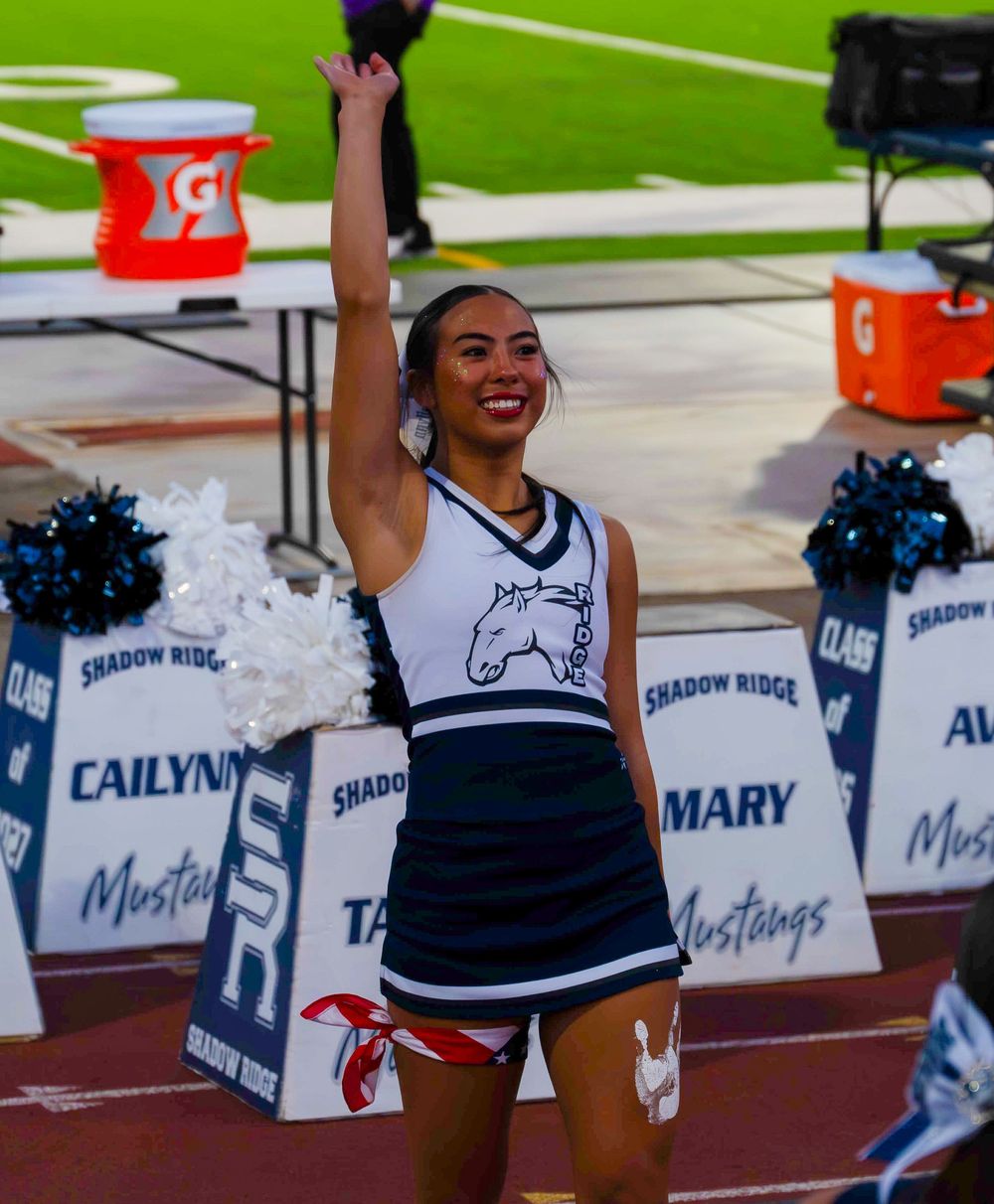 Shadow Ridge Mustangs cheerleader raising hand at a high school football game sideline.