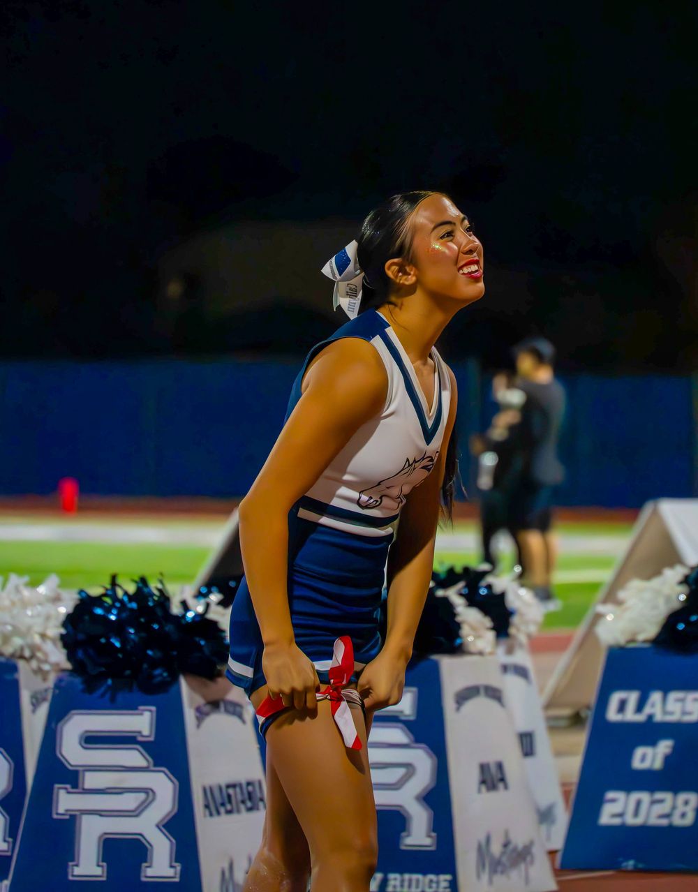 Shadow Ridge cheerleader performing at a night high school football game with SR banners.