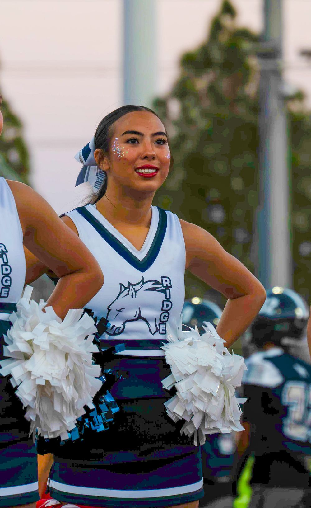 Shadow Ridge Mustangs cheerleader smiling with white pom-poms at a football game.