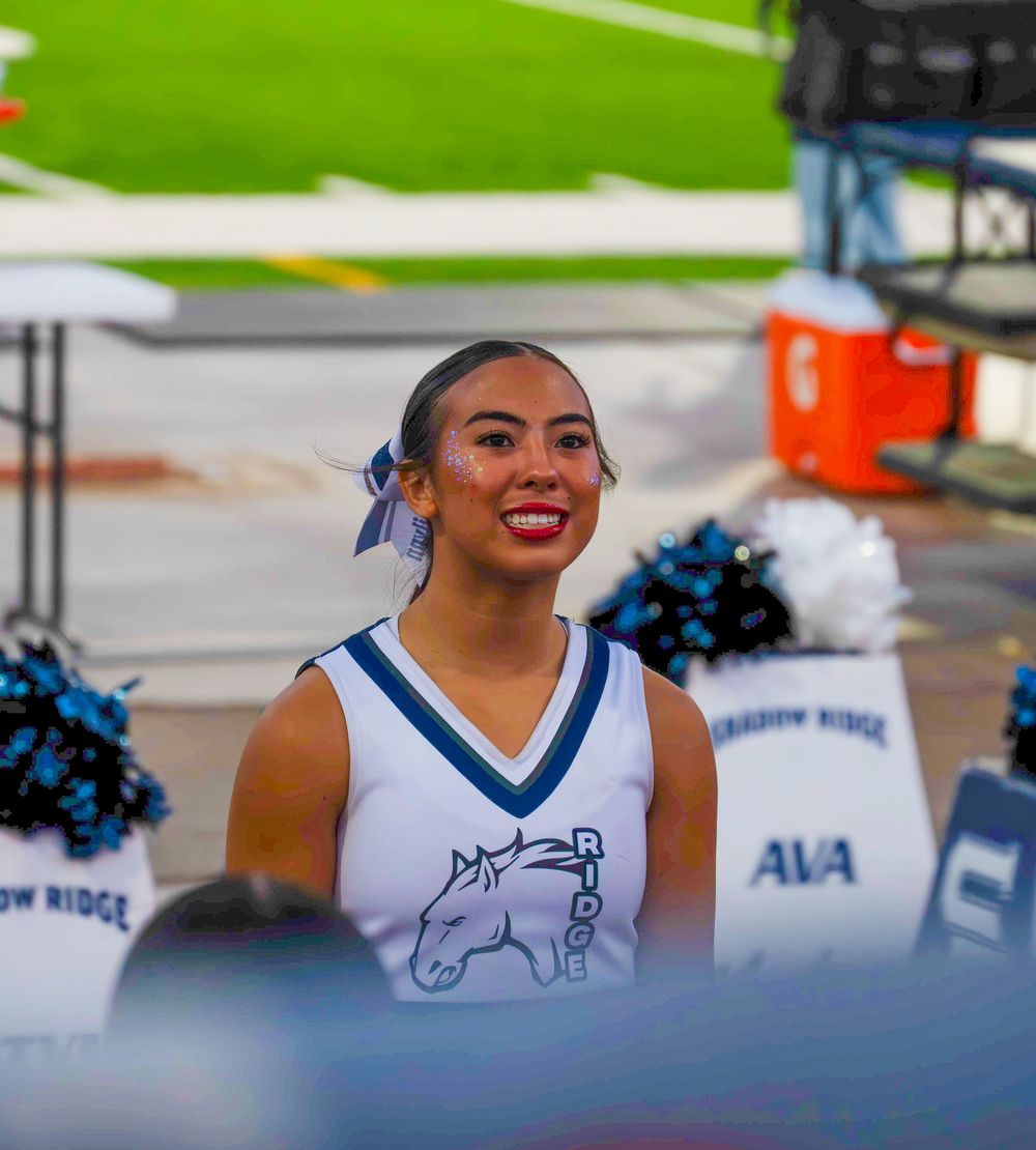 Smiling Shadow Ridge Mustangs cheerleader holding pom-poms at a high school football game.
