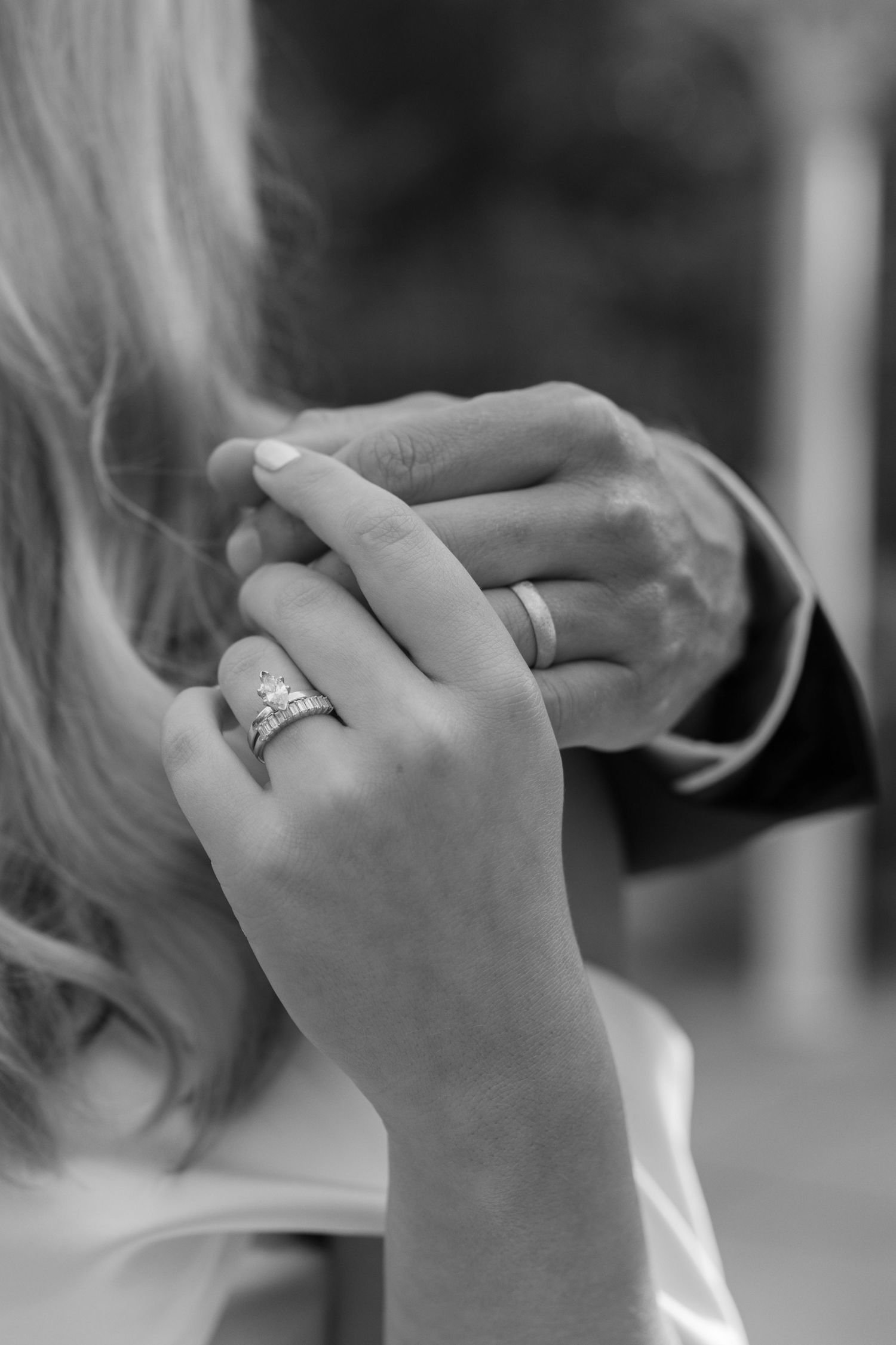 Black and white close-up of hands showing engagement ring and wedding band.