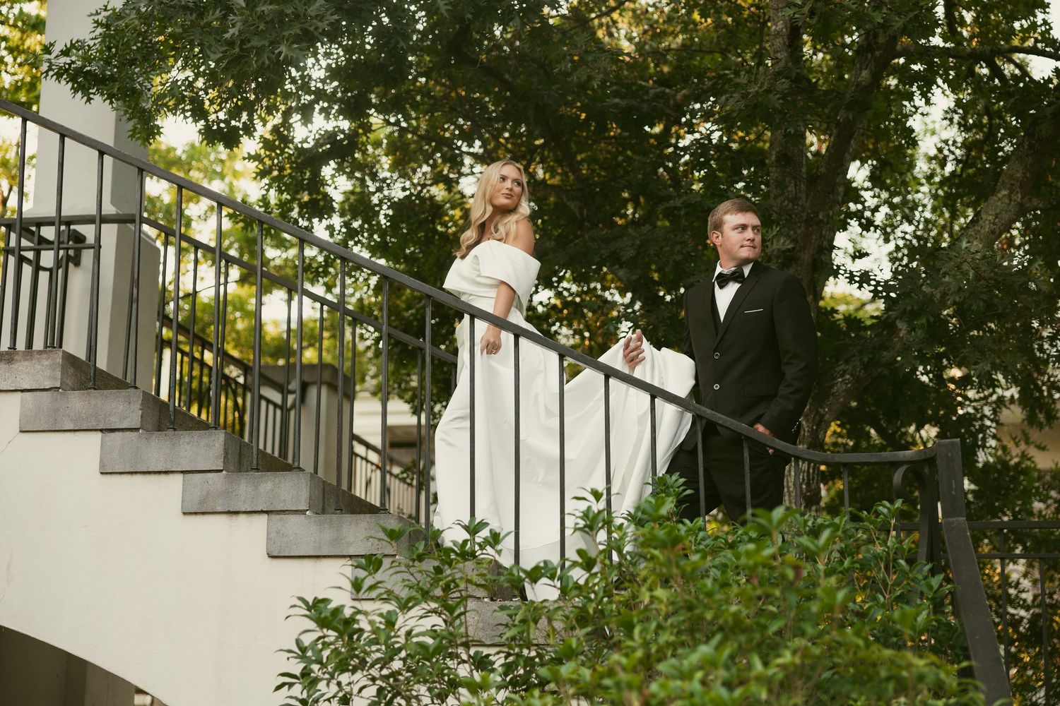 Wedding couple posing on outdoor staircase surrounded by greenery.