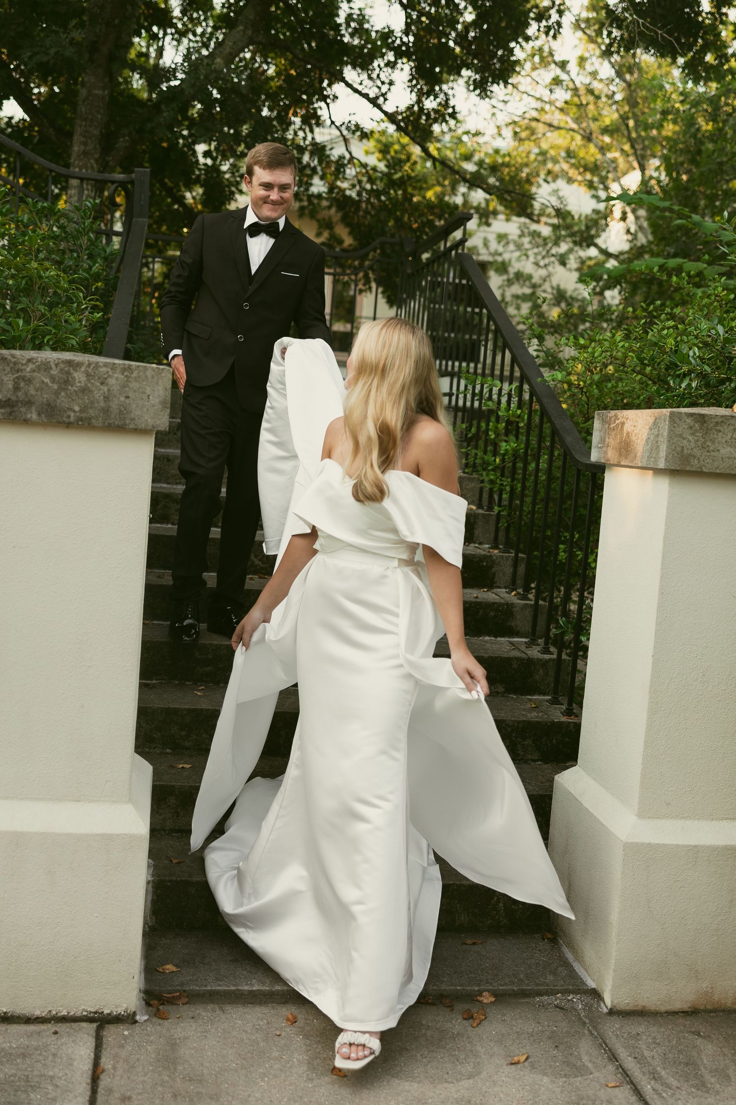Elegant wedding couple posing by white pillars and iron gates in garden setting.