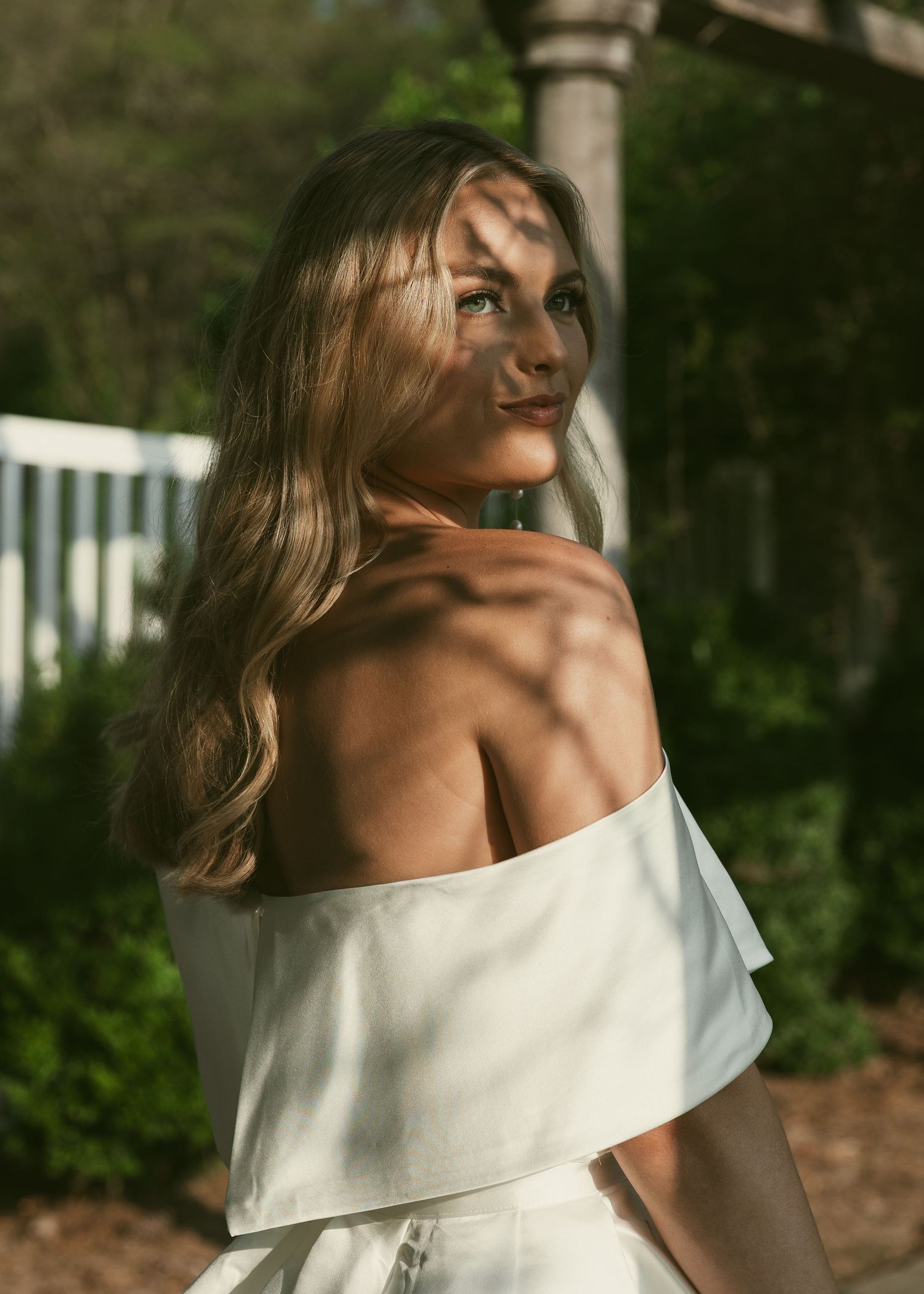Sunlit portrait showcasing off-shoulder wedding dress design in garden setting.