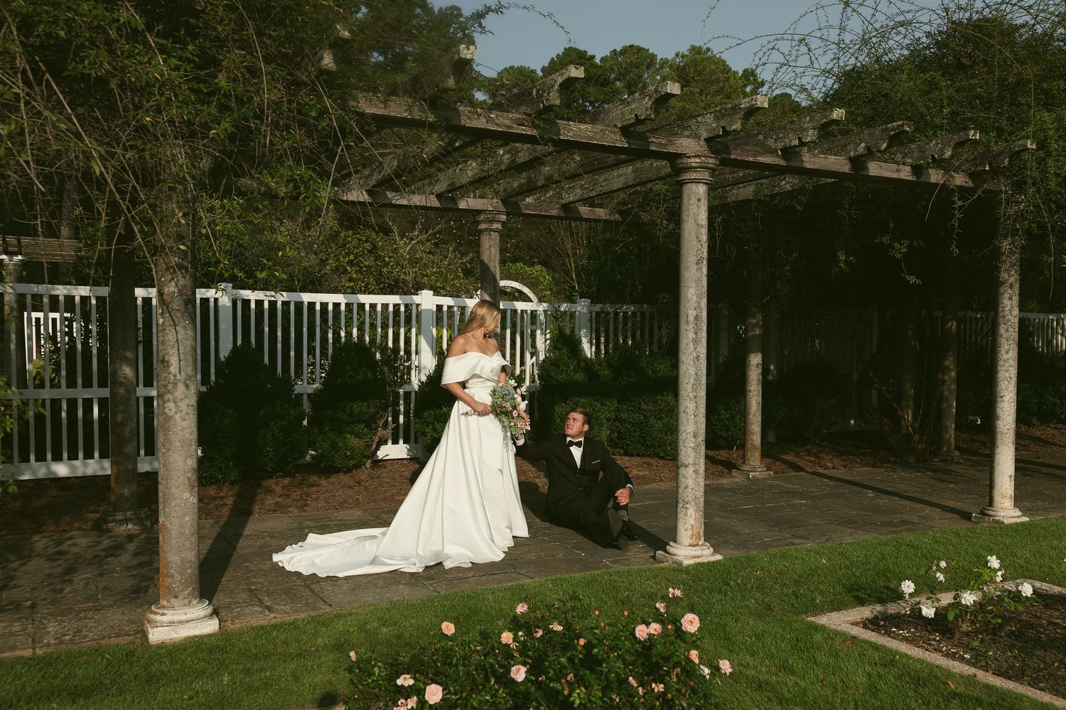 Wedding couple walking along white garden pergola with landscaped grounds.