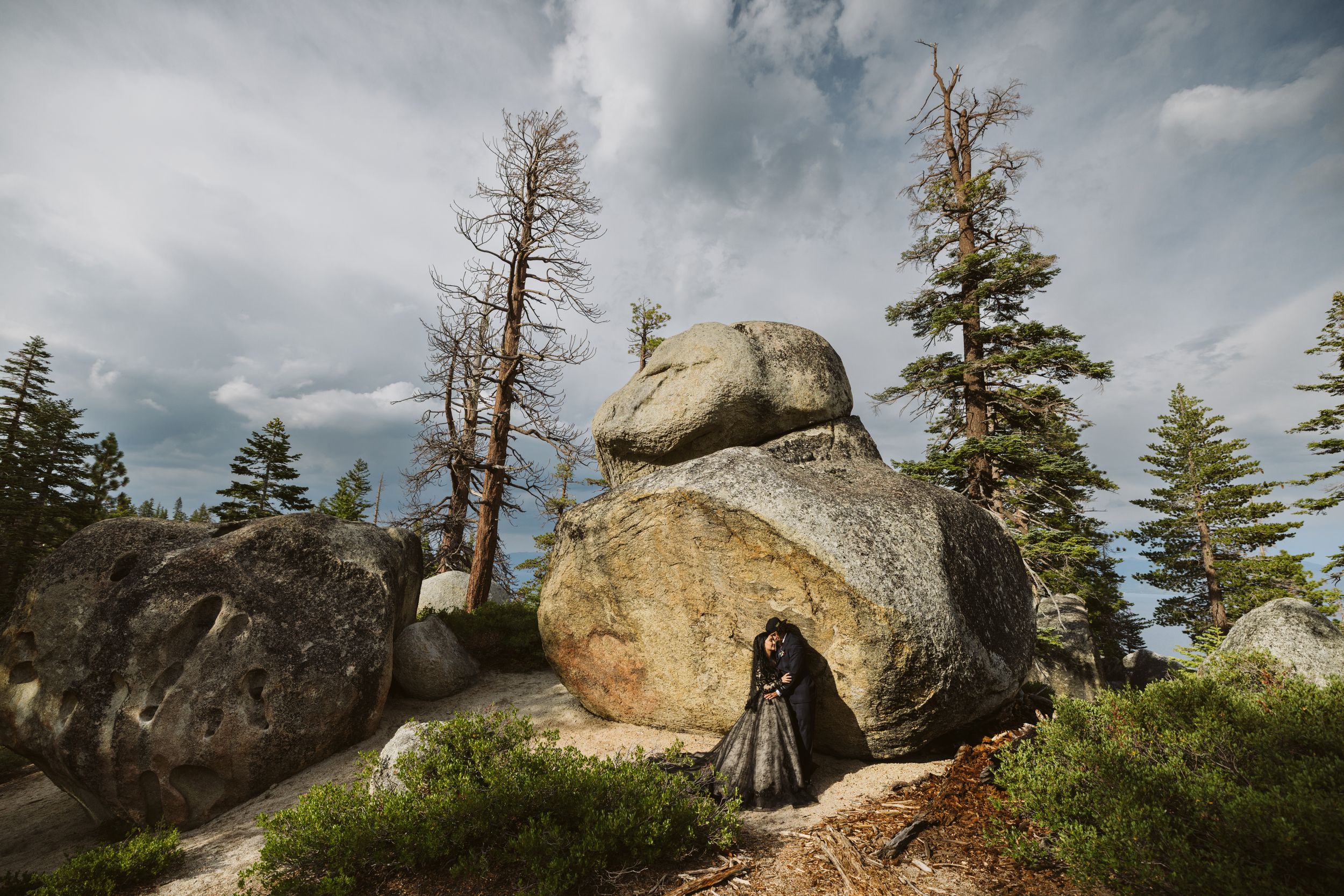 Rocky mountain landscape with weathered trees against cloudy sky.