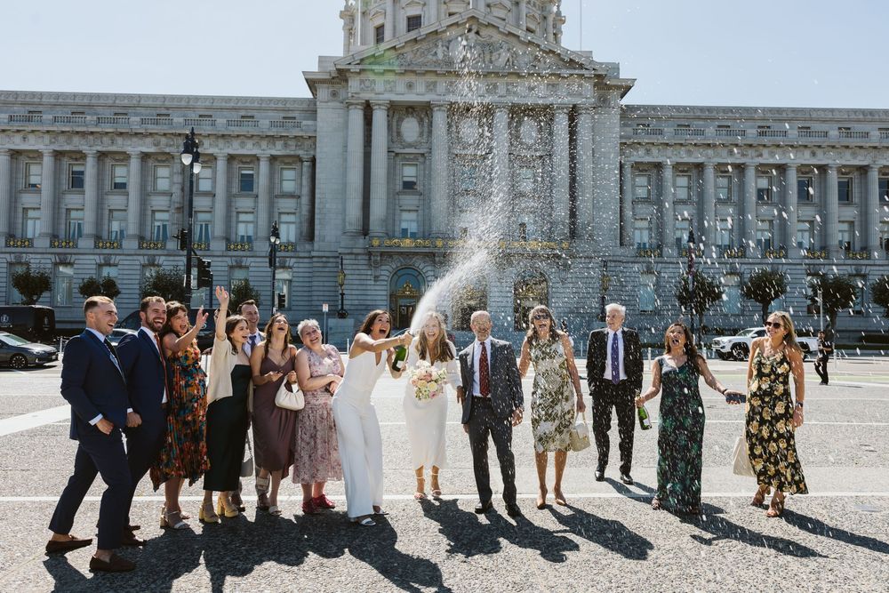 Wedding party gathering outside ornate classical building with grand architecture.