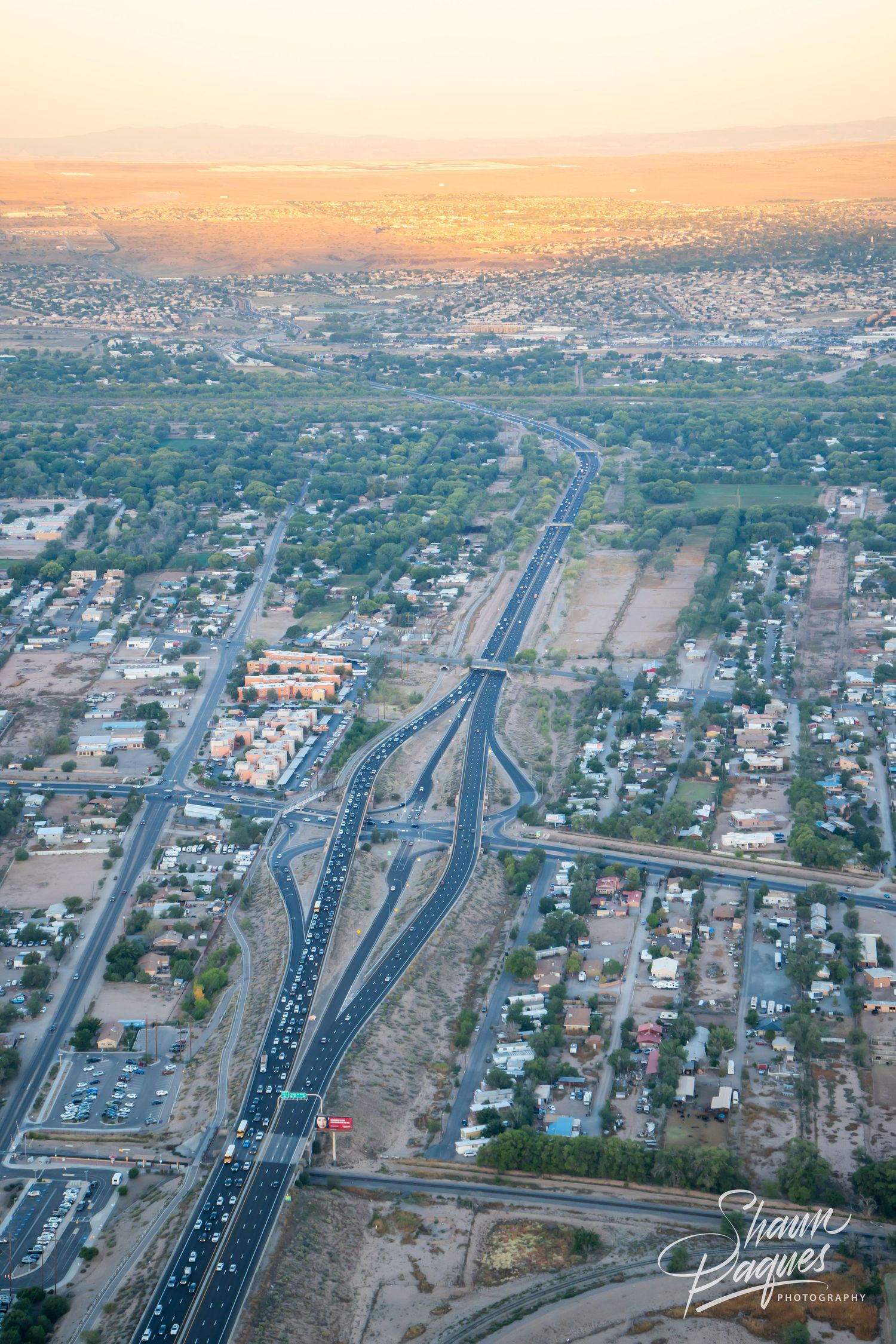 Aerial panoramic view of a highway interchange in an urban area during sunset with residential neighborhoods visible.