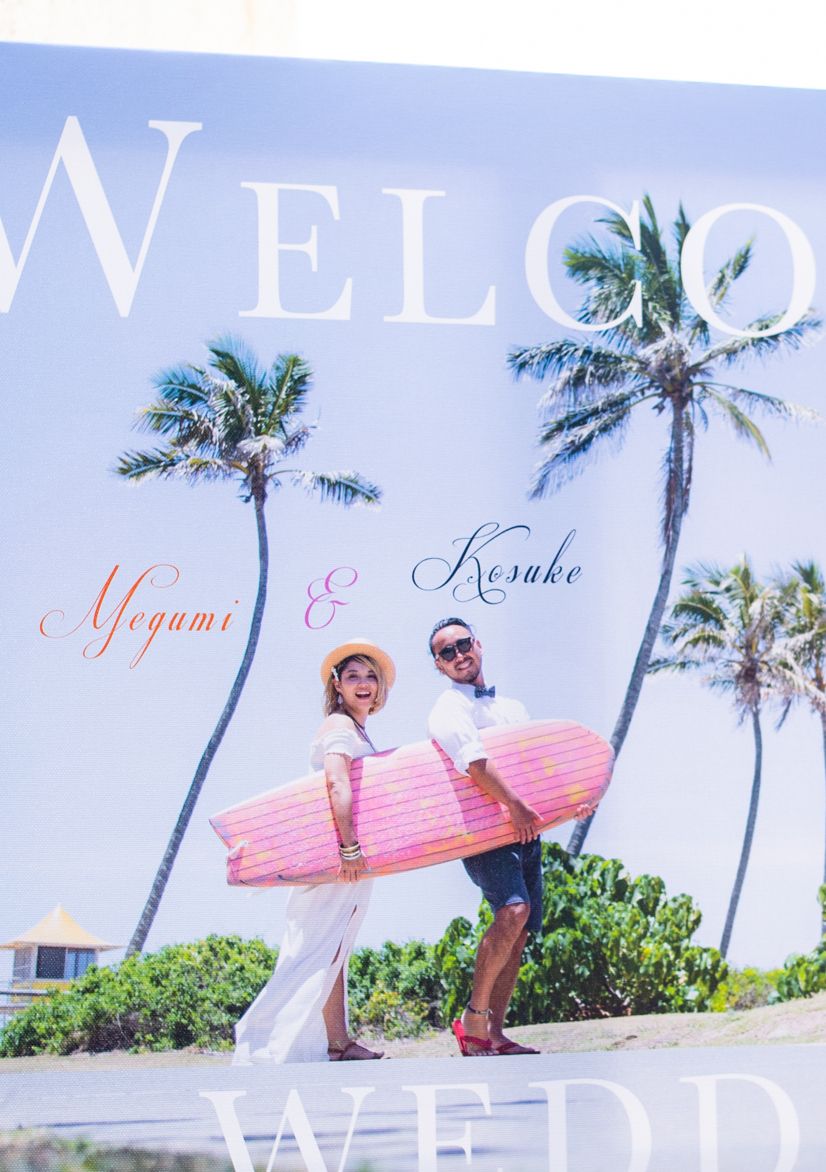 Couple holding a surfboard at a tropical beach wedding welcome sign for couple.