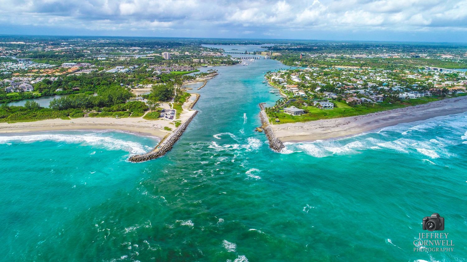 Aerial panoramic view of turquoise ocean waters, coastal development, and sandy beaches under cloudy skies.