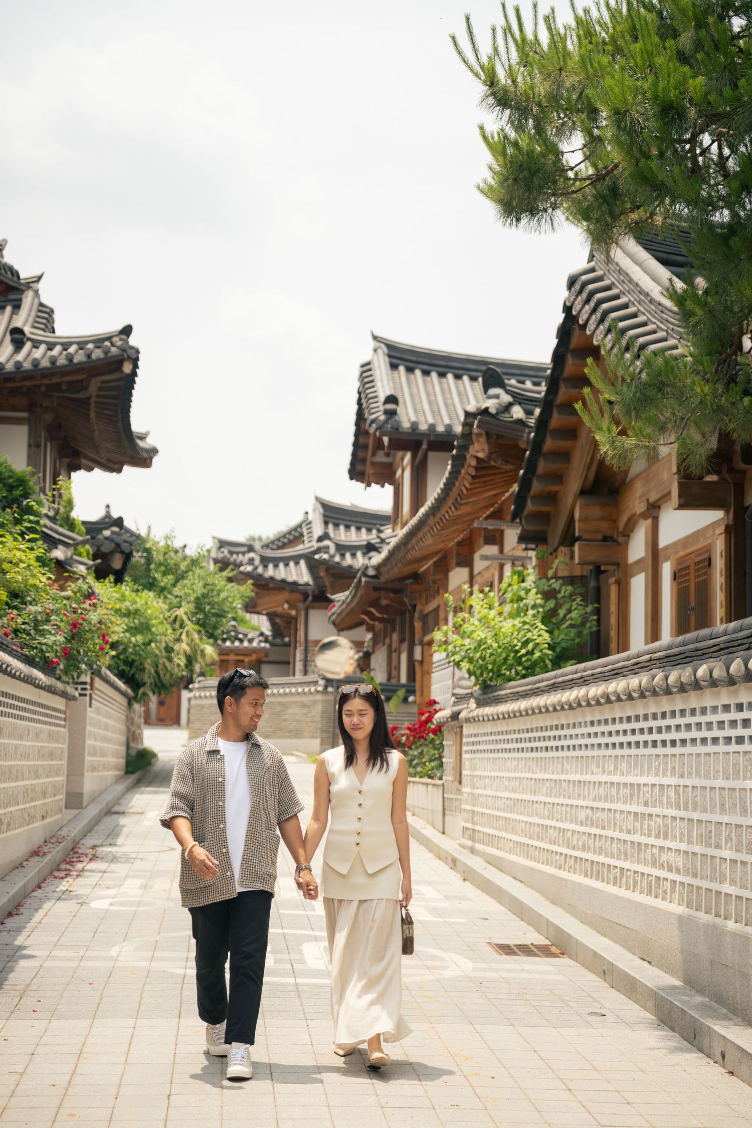 A couple strolls hand in hand along a traditional Korean alleyway with ornate tiled roofs and stone walls in Bukchon village.