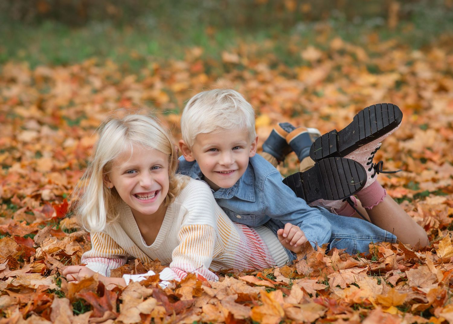 Children playing and lying in colorful autumn leaves on the ground during fall season.