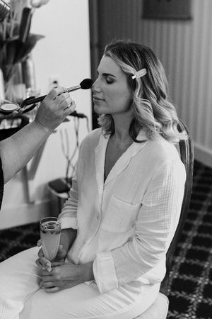 Series of black and white photos showing someone in white robe applying makeup while getting ready.