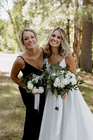 Bridesmaids in black dresses pose with white floral bouquets outdoors.