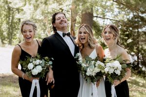 Wedding party laughs together while holding white floral bouquets outdoors.