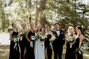 A wedding party poses together outdoors among pine trees in formal black and white attire.