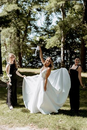 A couple shares joyful moments while holding a white wedding dress veil in a sunny outdoor setting with pine trees.