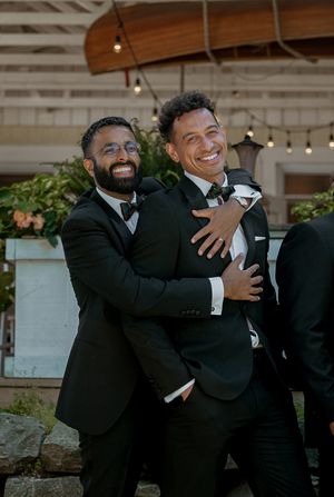 Groomsmen in black tuxedos share joyful embraces and laughter during wedding photo session.