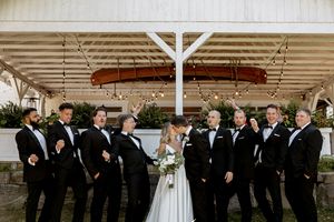 Wedding party in formal attire poses under covered outdoor venue.