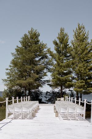 White wedding ceremony setup with chairs and aisle overlooking evergreen trees against blue sky.