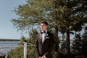 A romantic waterfront wedding ceremony scene with a white pillar and trees framing the scenic view.