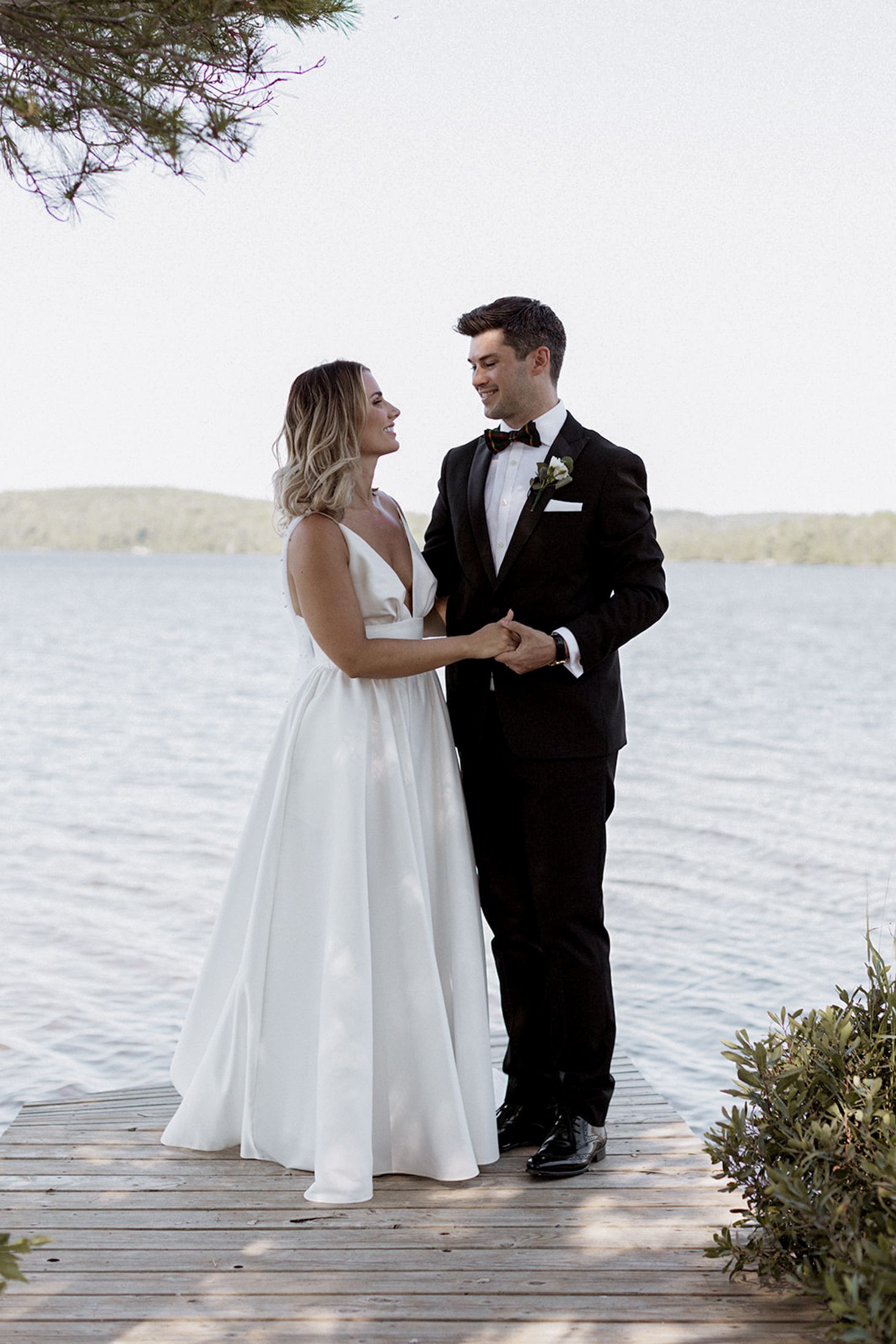 Wedding couple shares intimate moments on wooden dock overlooking serene waterfront.