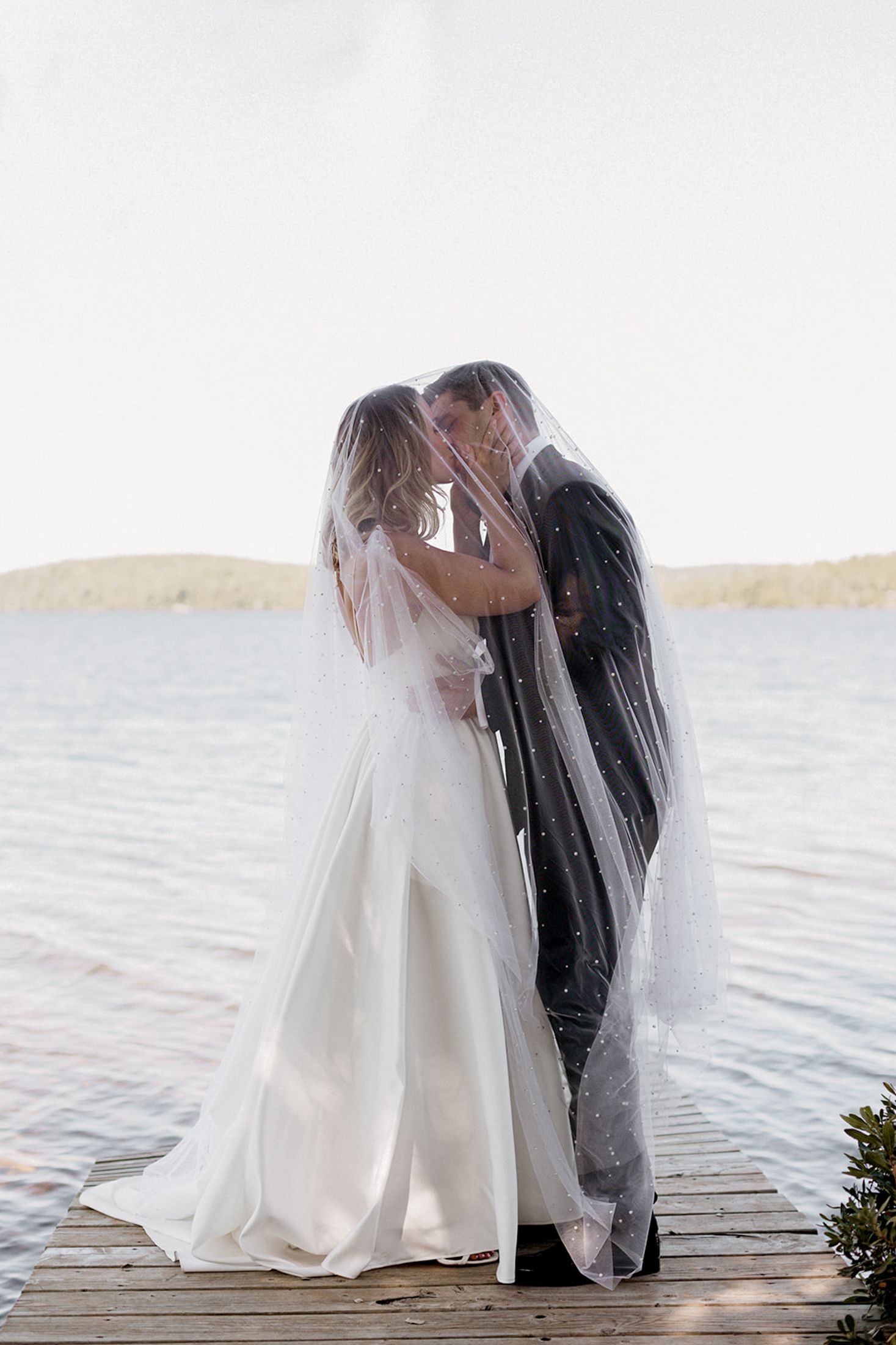 Romantic wedding couple shares an intimate moment on a wooden dock at sunset by the water.
