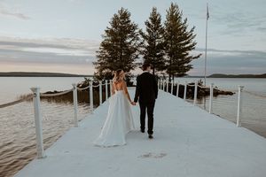 Wedding party walks along a snowy boardwalk with pine trees and water views.