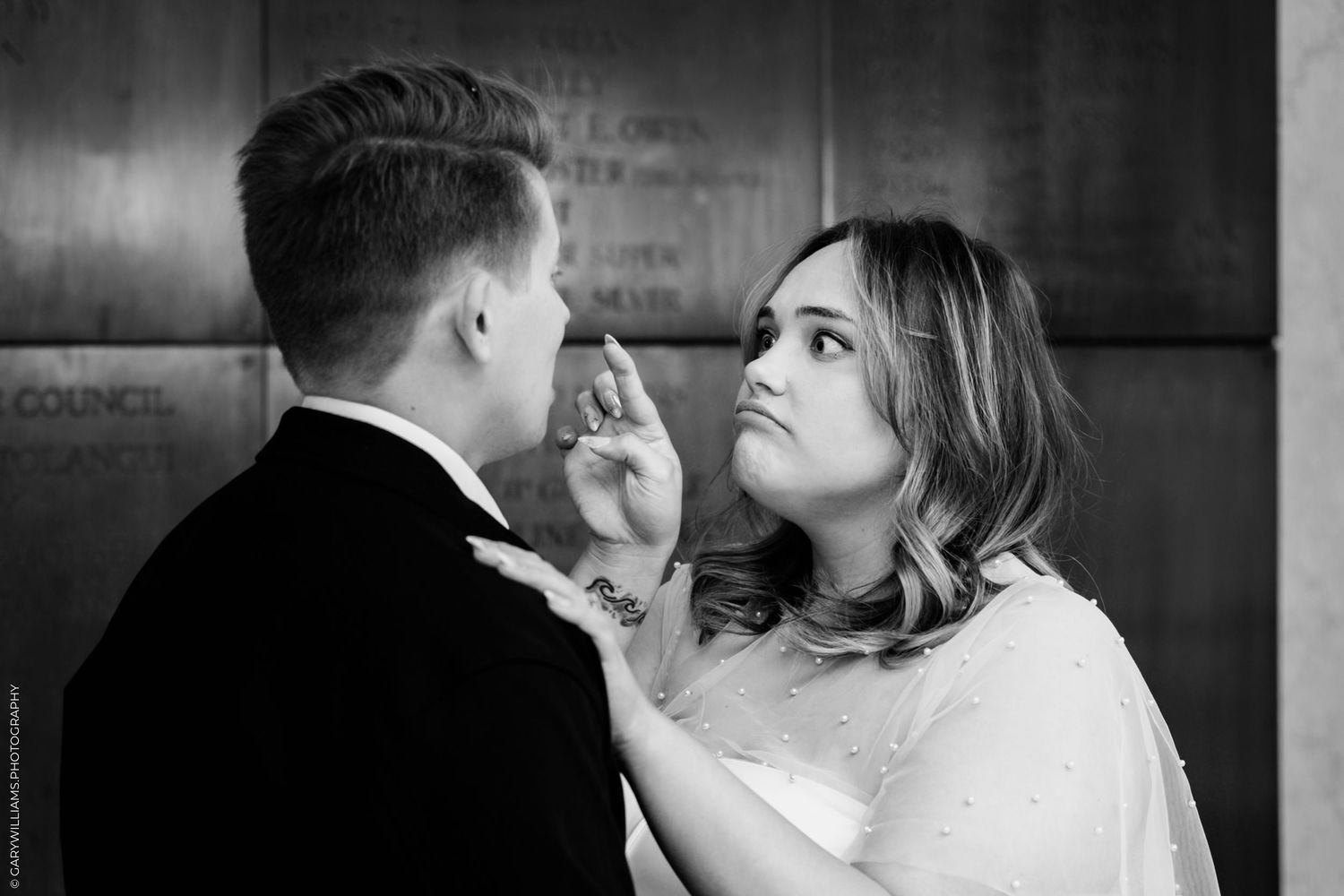 A tender moment between a couple in formal attire against a dark wooden wall.
