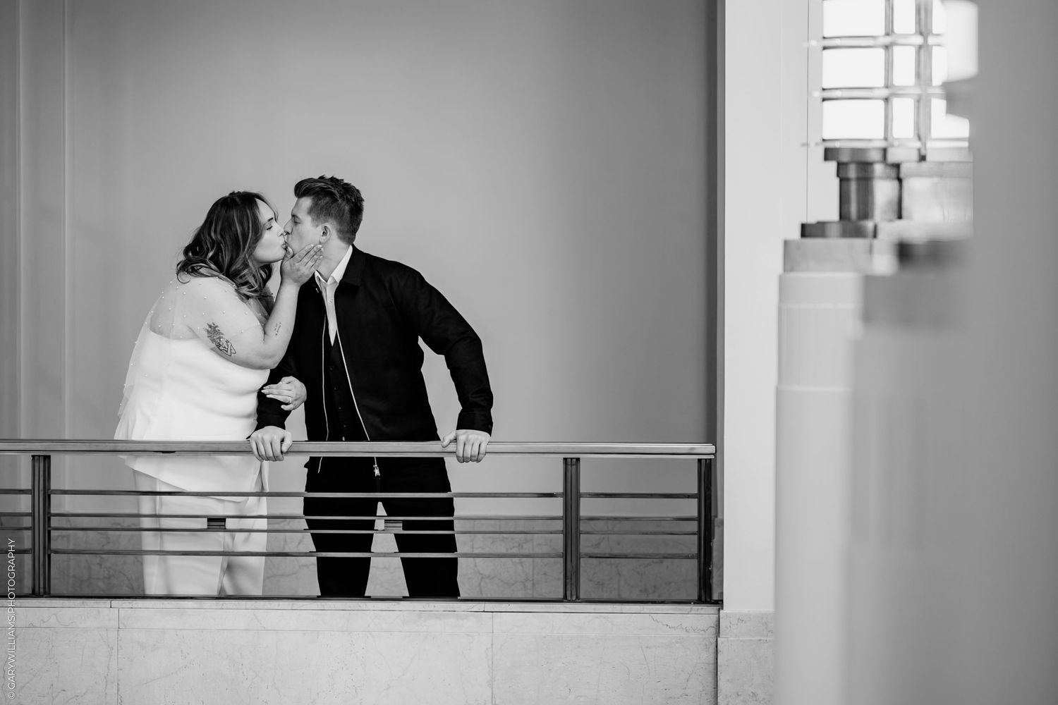 A romantic black and white wedding moment captured on a modern balcony with metal railings.