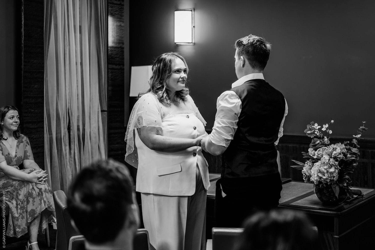 Black and white photo of people dancing and celebrating at an indoor event with curtains and lighting.