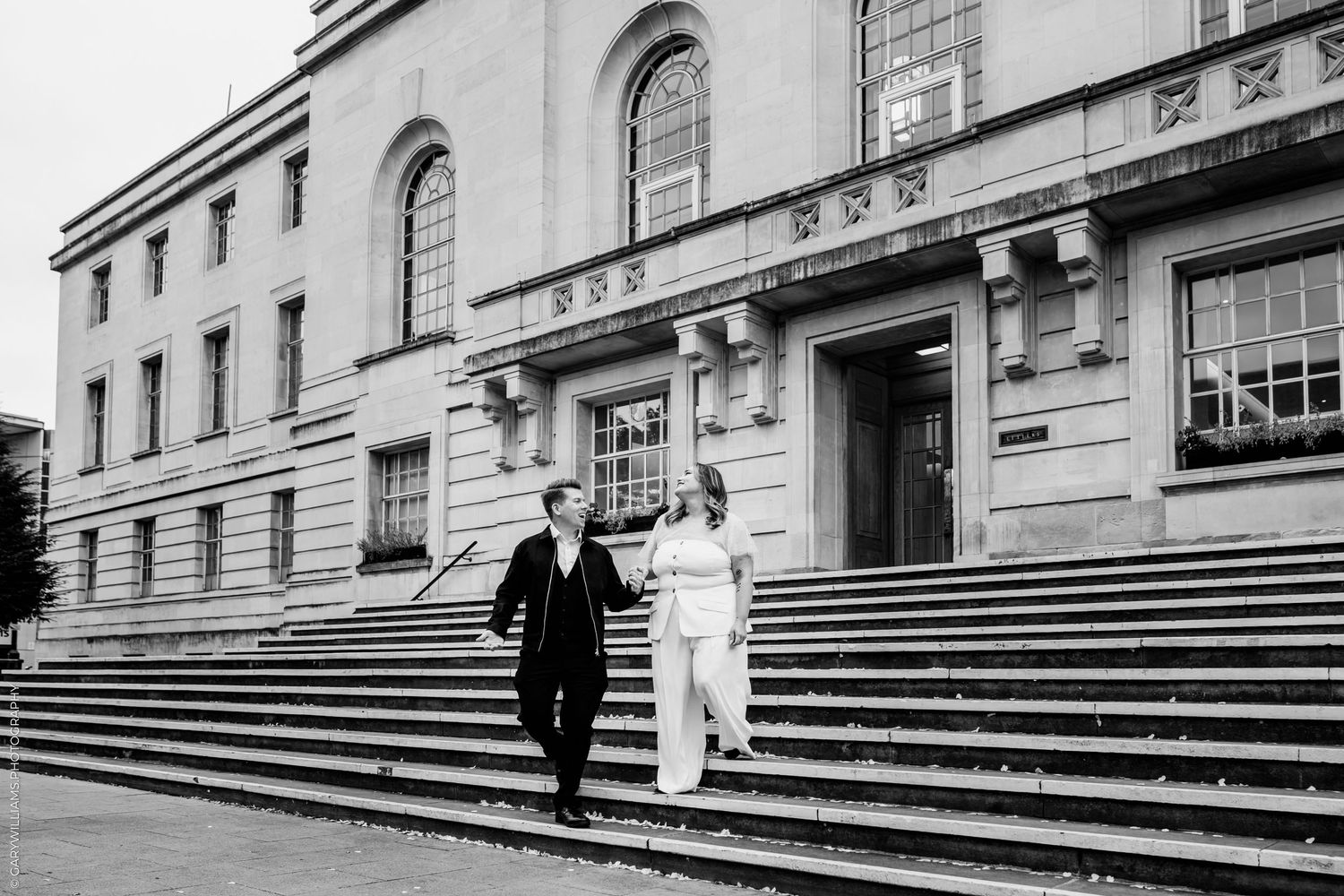 A black and white photo of a couple descending grand stone steps outside a stately building.