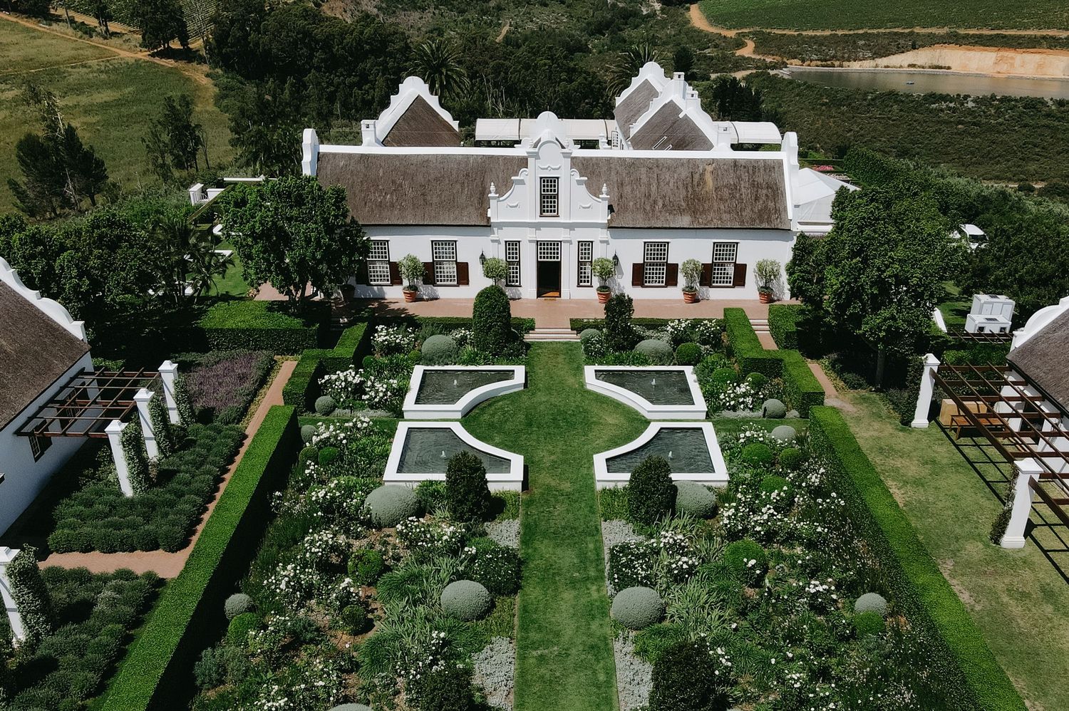 Aerial view of a grand white colonial estate with manicured gardens and symmetrical landscaping in South Africa.