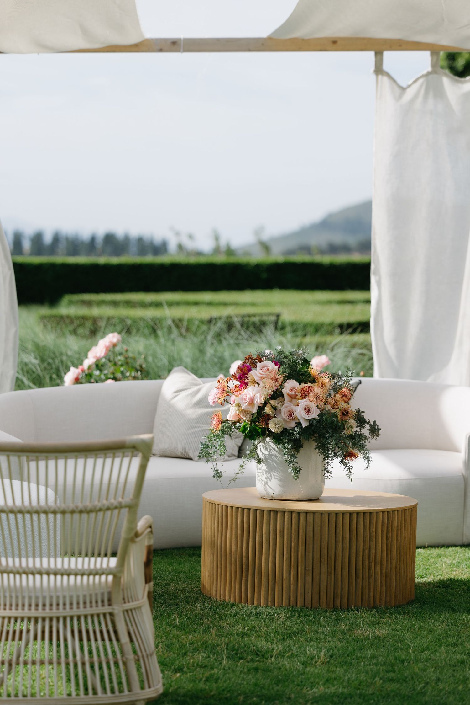 Modern outdoor seating arrangement featuring white cushioned chairs and round wooden tables adorned with floral centerpieces.