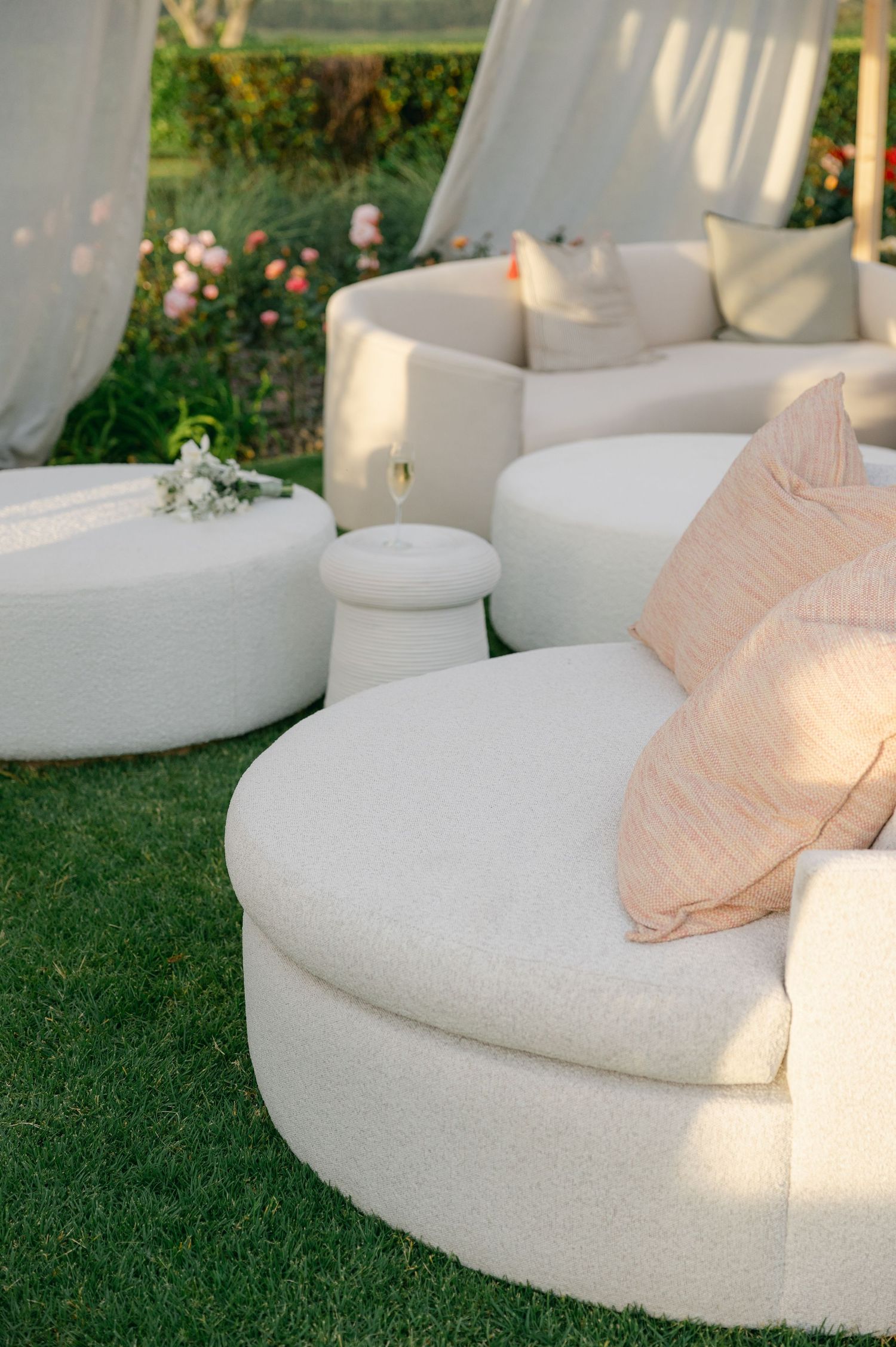 Luxurious white curved lounge seating with blush pillows arranged on a manicured lawn for outdoor event.