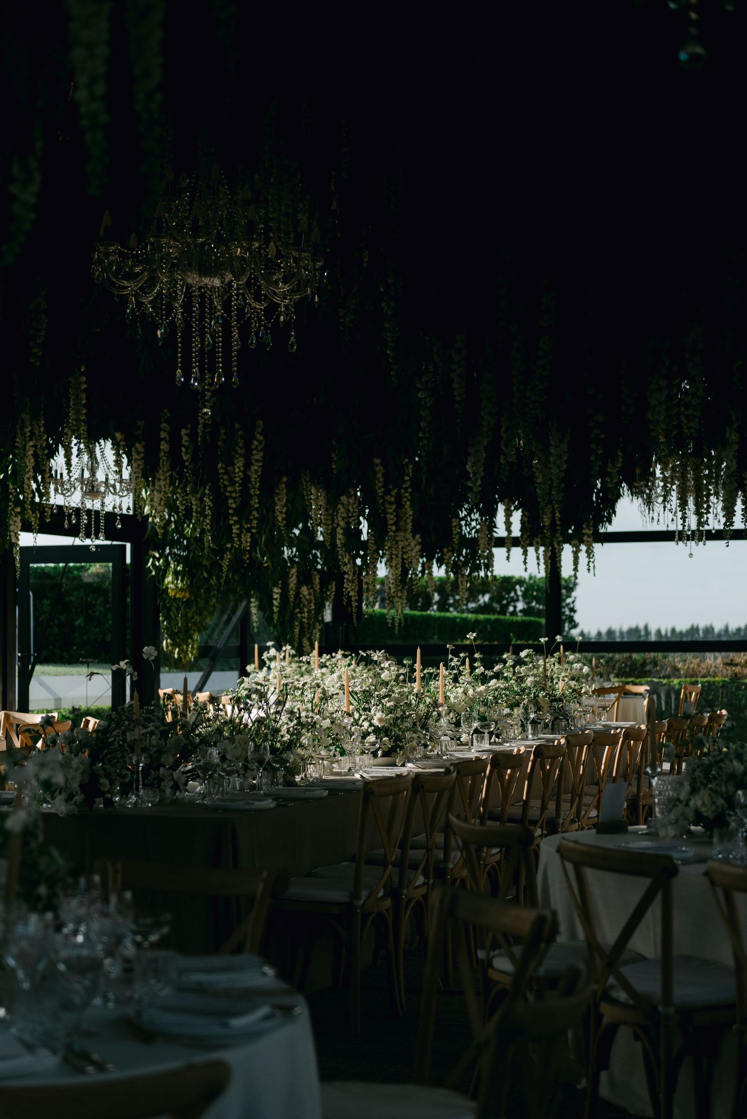 Romantic indoor reception venue with hanging floral installations and crystal chandeliers over dining tables.
