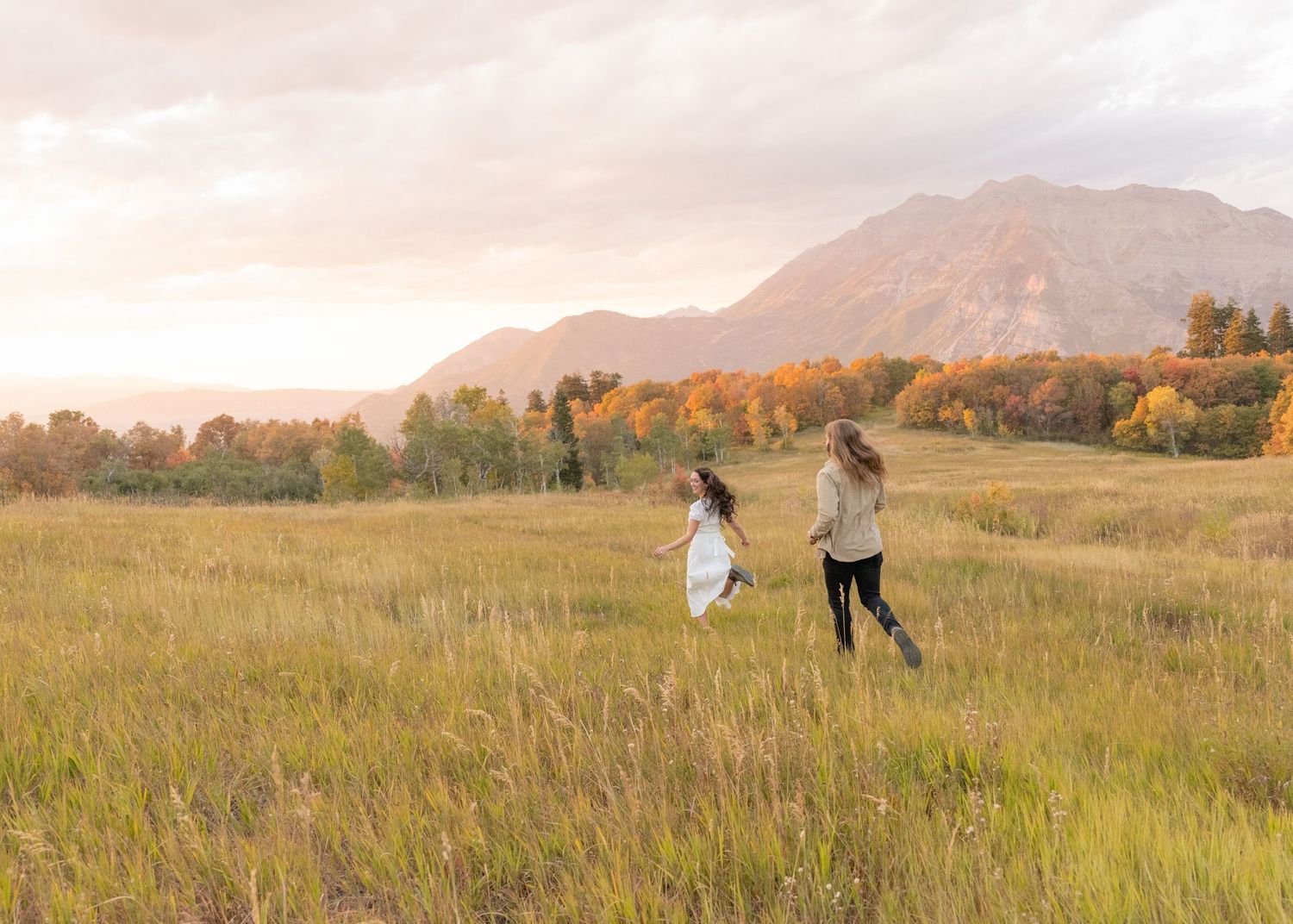 People walking together through a golden autumn meadow with mountains in the background at sunset.