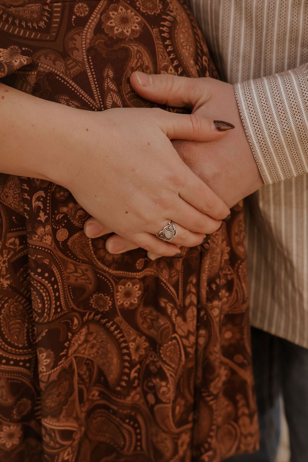 Close-up detail of hands against brown paisley patterned fabric.