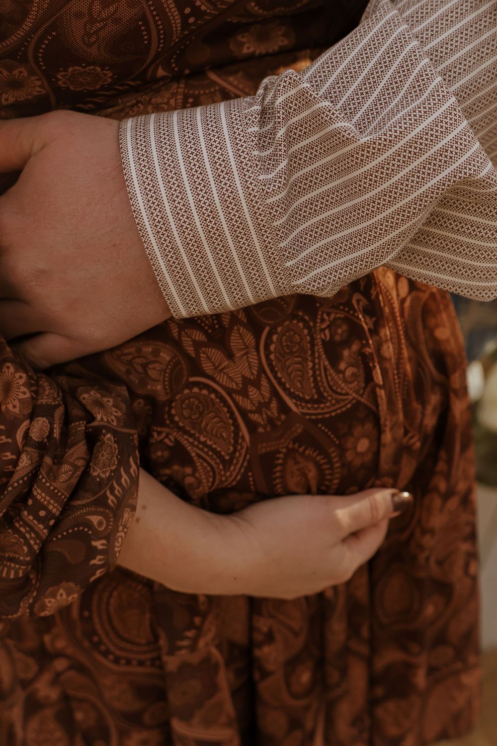 Close-up of hands cradling a baby bump in a brown paisley dress with striped sleeve detail.