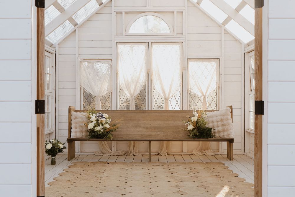 White chapel interior with wooden bench and floral arrangements near diamond-paned windows.
