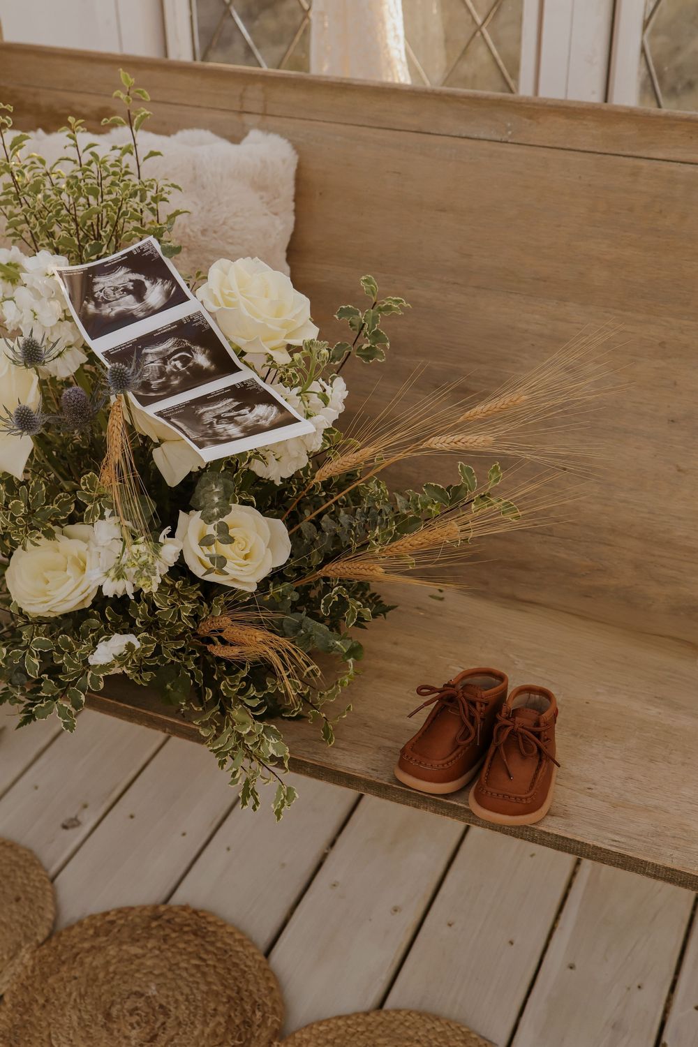 Baby shoes next to floral arrangement with ultrasound photos on wooden bench.