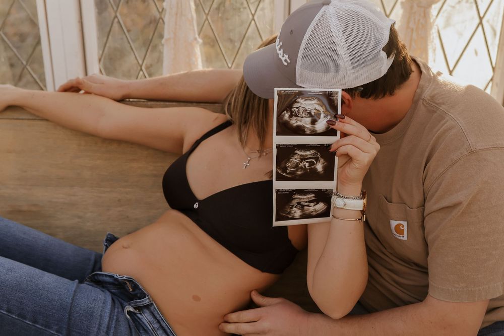 Maternity photoshoot featuring ultrasound photos in casual setting.